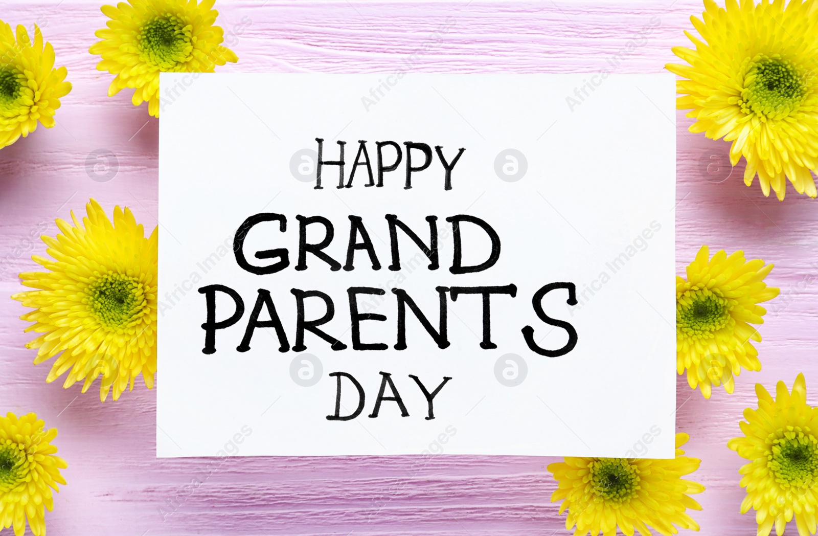 Photo of Beautiful yellow flowers and card with phrase Happy Grandparents Day on pink wooden background, flat lay