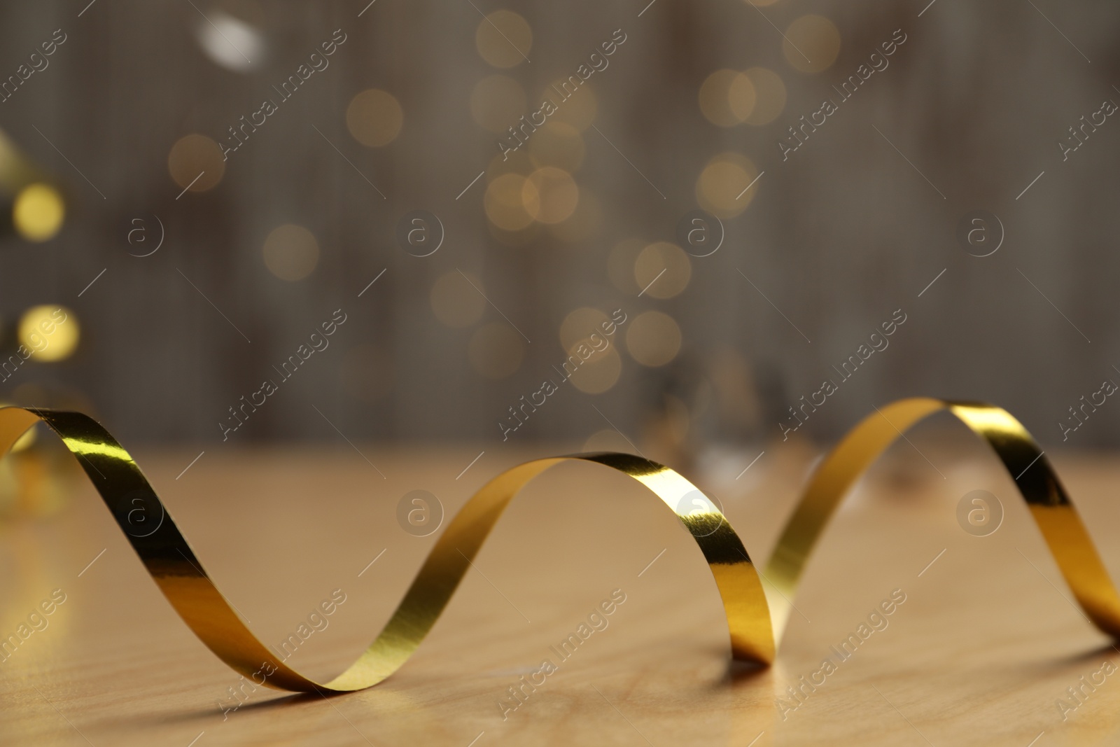 Photo of Shiny golden serpentine streamer on wooden table against blurred lights, closeup. Space for text