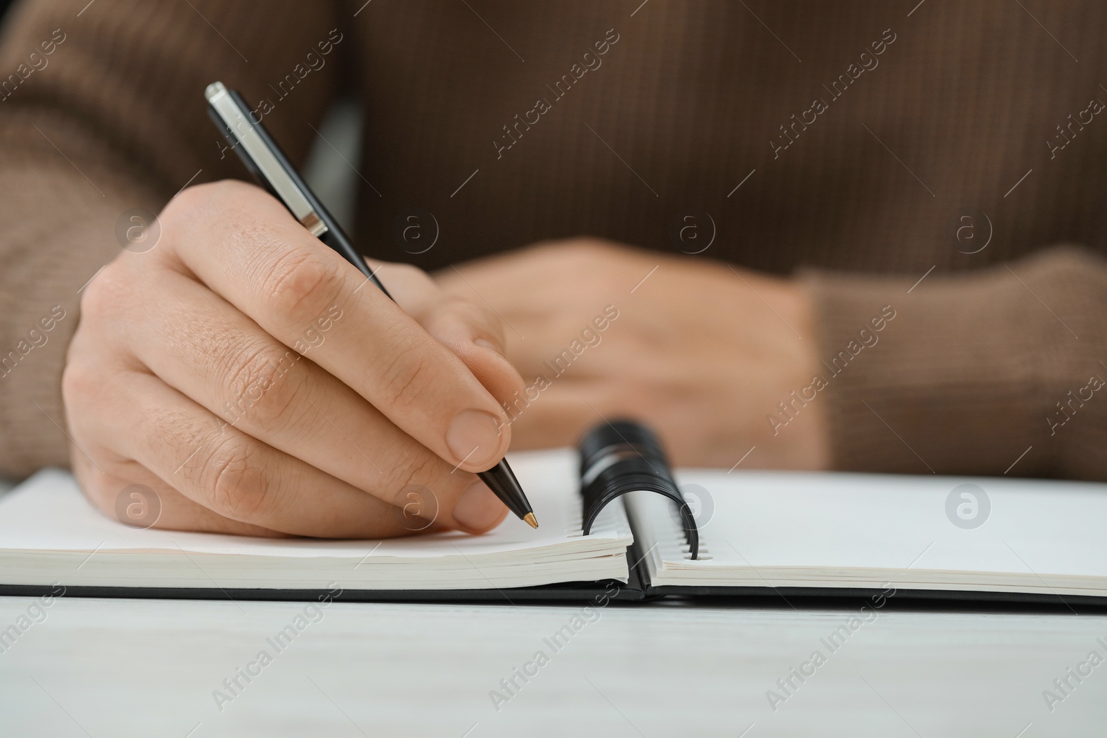 Photo of Man writing in notebook at white table, closeup. Space for text