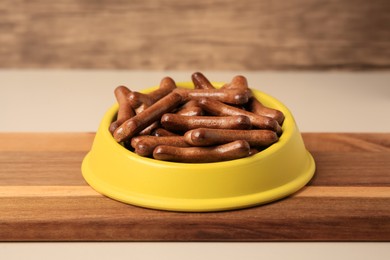 Yellow bowl with bone shaped dog cookies on wooden board