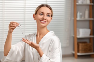 Photo of Beautiful woman applying cosmetic serum onto her hand in bathroom, space for text