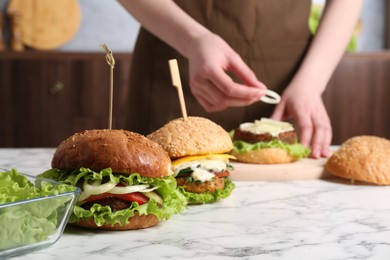 Photo of Woman making delicious vegetarian burger at white marble table, selective focus