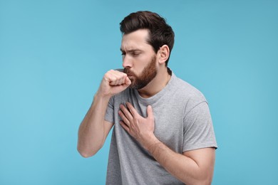 Photo of Sick man coughing on light blue background. Cold symptoms