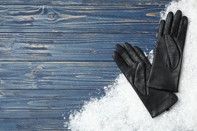 Photo of Stylish black leather gloves and artificial snow on blue wooden table, top view. Space for text