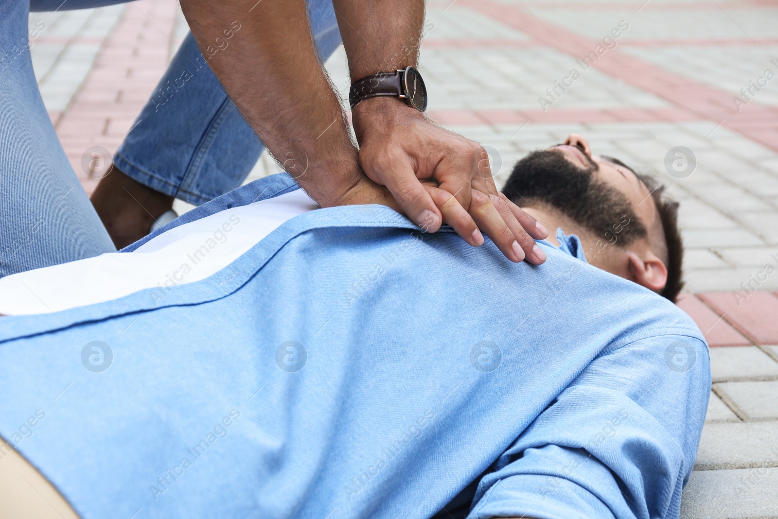 Photo of Passerby performing CPR on unconscious young man outdoors, closeup. First aid