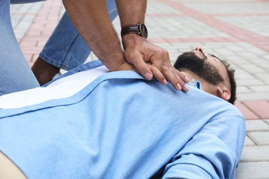 Photo of Passerby performing CPR on unconscious young man outdoors, closeup. First aid