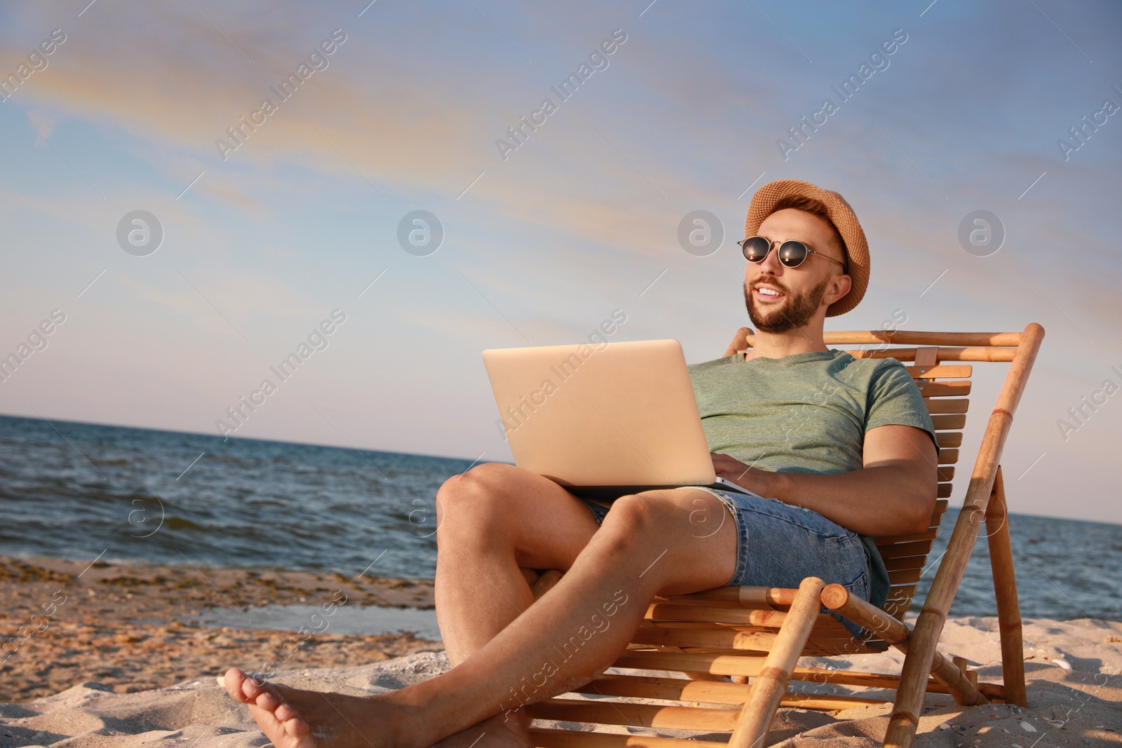 Photo of Man working with laptop in deck chair on beach