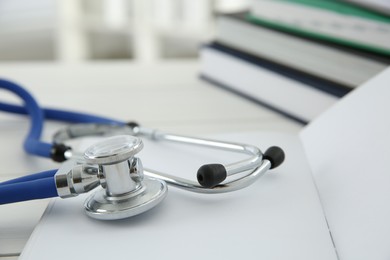 Photo of One new medical stethoscope and books on white table, closeup