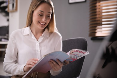 Photo of Happy woman reading interesting magazine in office