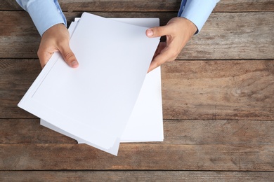 Photo of Man holding blank paper sheets for brochure at wooden table, top view. Mock up