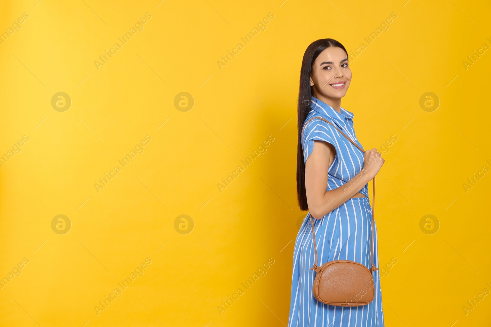 Photo of Beautiful young woman with stylish bag on orange background, space for text