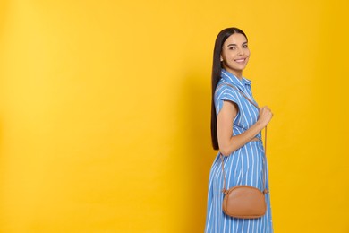 Beautiful young woman with stylish bag on orange background, space for text