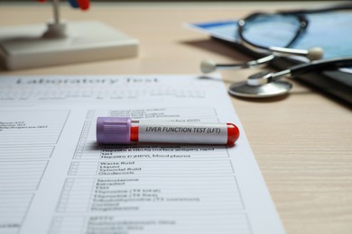 Liver Function Test. Tube with blood sample and laboratory form on wooden table, closeup