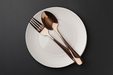 Clean plate, fork and spoon on black table, top view