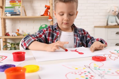 Little boy painting with finger at white table indoors