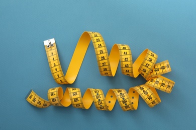 Yellow measuring tape on light blue background, top view