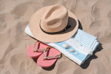 Photo of Straw hat, beach towel, seashells and flip flops on sand