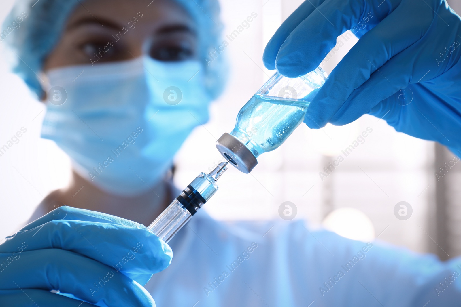 Photo of Woman filling syringe with vaccine from vial on blurred background, closeup