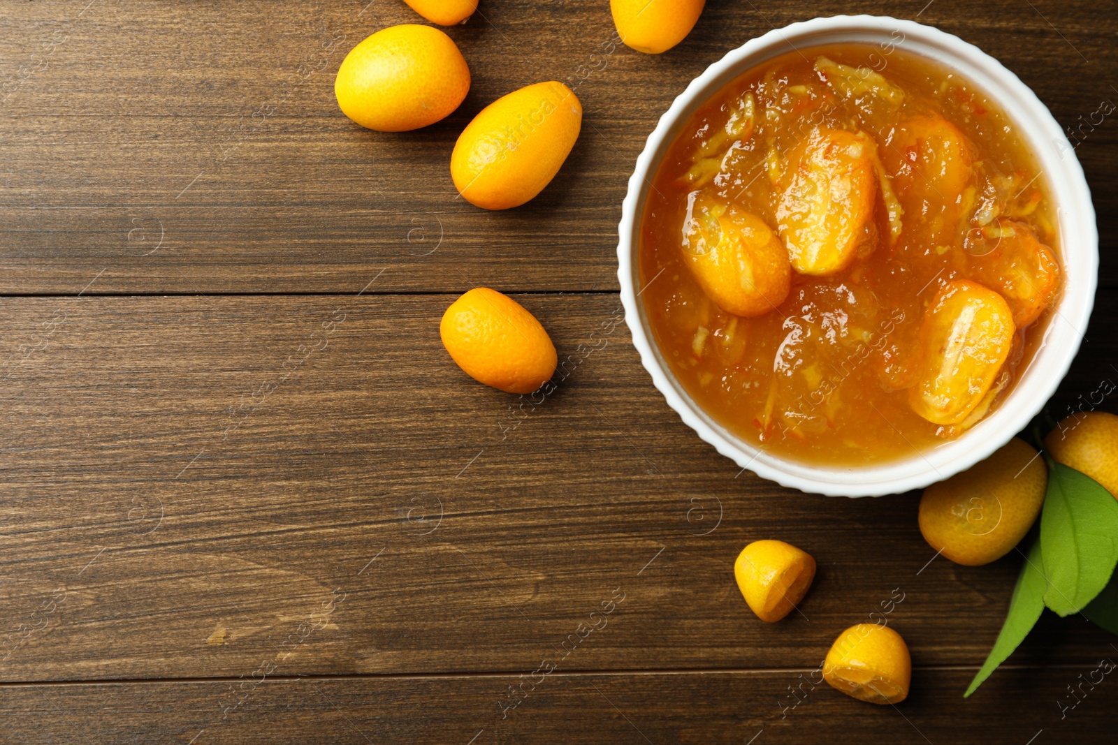 Photo of Delicious kumquat jam in bowl and fresh fruits on wooden table, flat lay. Space for text