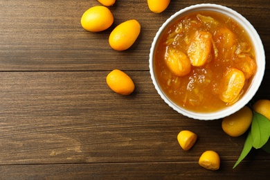 Photo of Delicious kumquat jam in bowl and fresh fruits on wooden table, flat lay. Space for text
