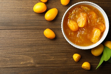 Delicious kumquat jam in bowl and fresh fruits on wooden table, flat lay. Space for text