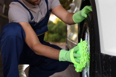 Photo of Worker washing auto wheel with sponge at outdoor car wash, closeup