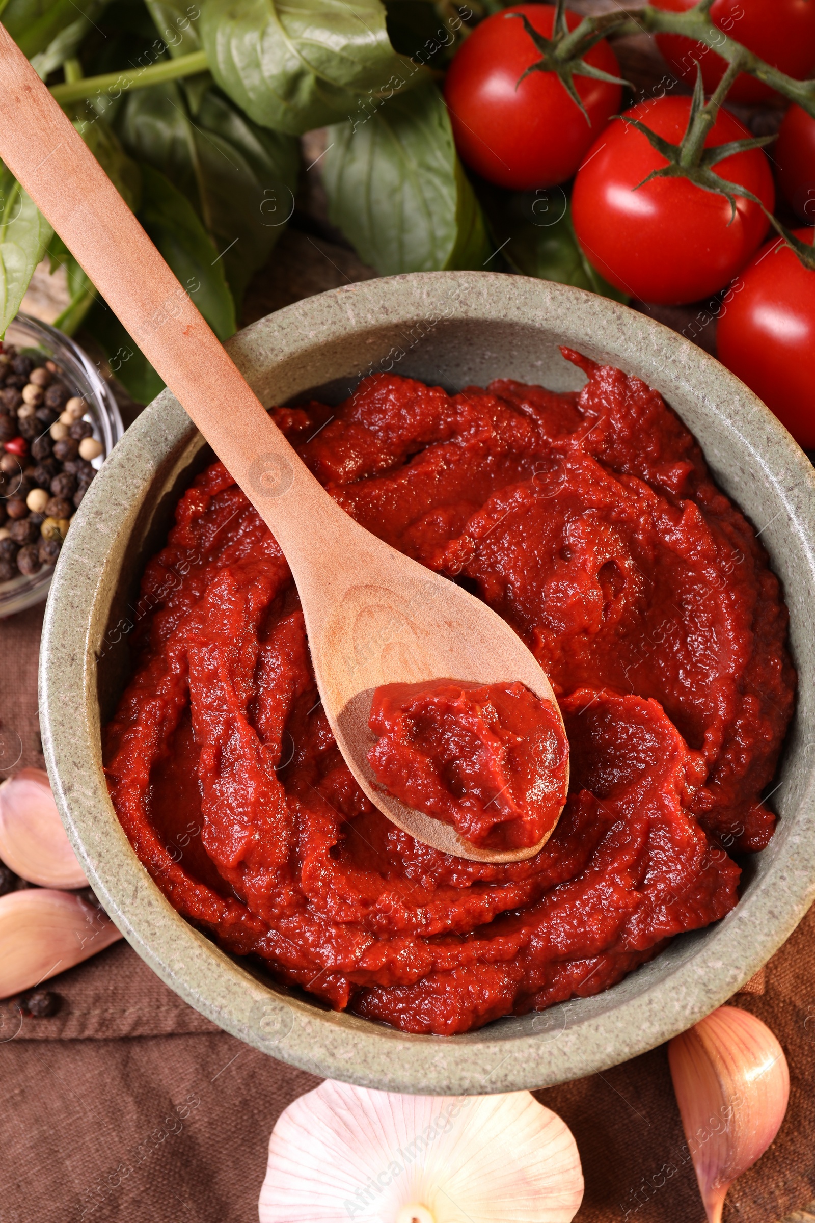 Photo of Bowl of tasty tomato paste with spoon and ingredients on table, flat lay