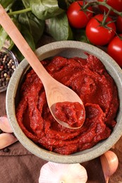 Bowl of tasty tomato paste with spoon and ingredients on table, flat lay