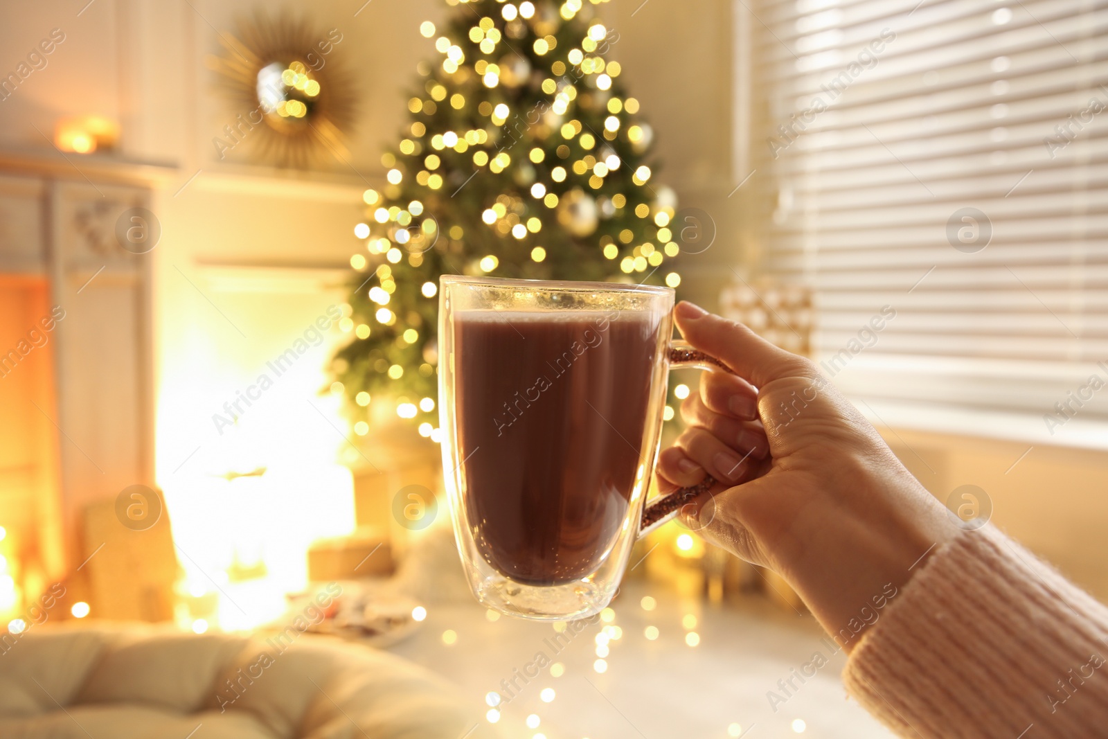 Photo of Woman with cup of drink and blurred Christmas tree on background, closeup