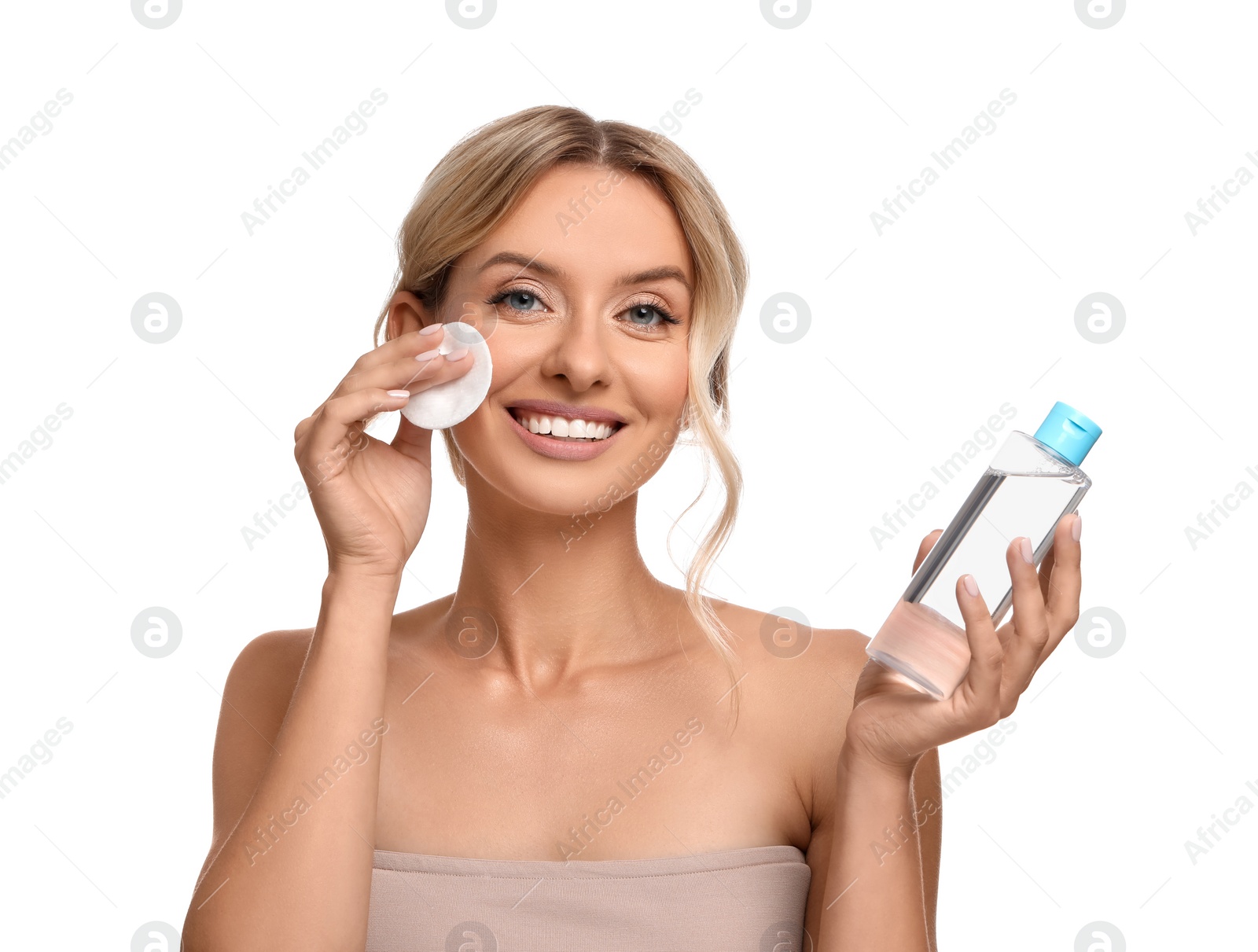 Photo of Smiling woman removing makeup with cotton pad and holding bottle on white background