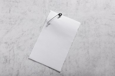 Sheet of paper attached with safety pin on grey textured background, top view