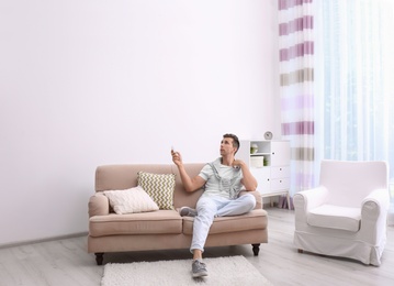 Photo of Young man operating air conditioner with remote control at home