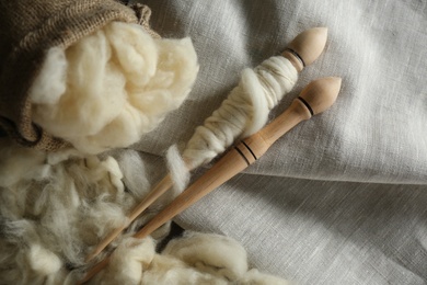 Photo of Soft white wool with spindle on fabric, flat lay