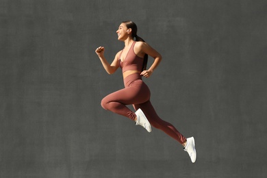 Photo of Young woman in stylish sports wear jumping on grey background