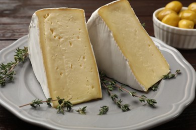 Photo of Pieces of tasty camembert cheese and thyme on table, closeup