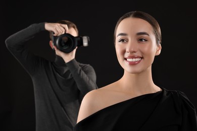 Photo of Photographer taking picture of beautiful woman on black background, selective focus