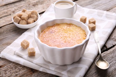 Delicious creme brulee in bowl, sugar cubes and spoon on wooden table, closeup