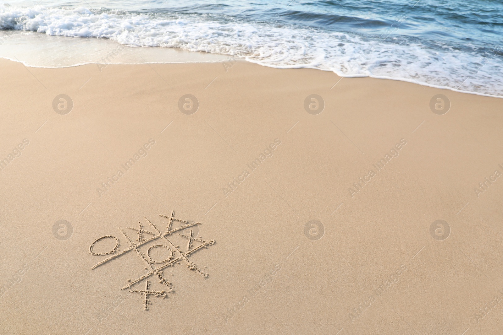 Photo of Tic tac toe game drawn on sand near sea, space for text