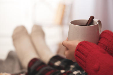 Photo of Woman holding cup of mulled wine indoors, closeup. Winter drink