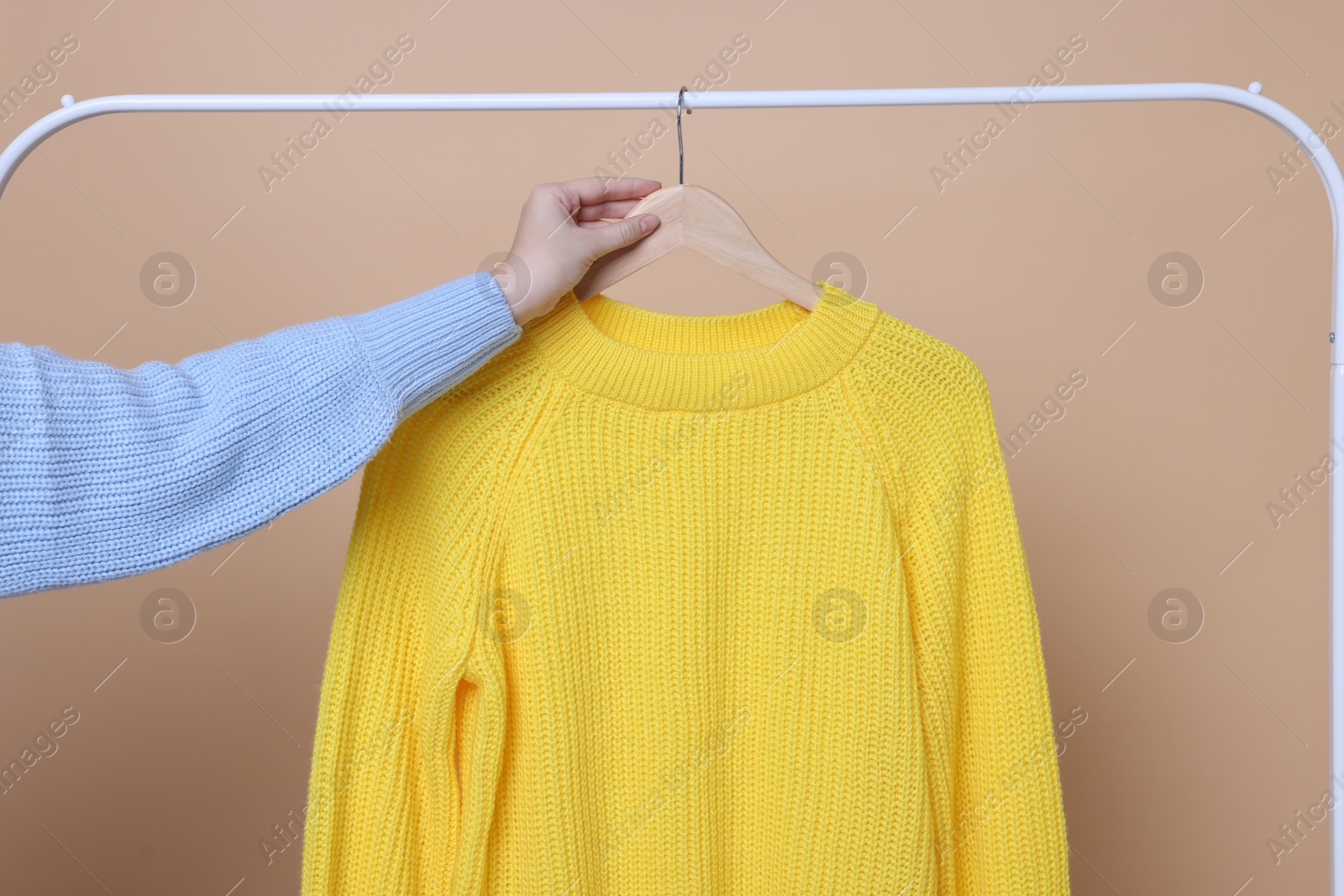 Photo of Woman taking yellow sweater from rack on beige background, closeup