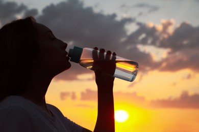 Photo of Young woman drinking water to prevent heat stroke outdoors at sunset