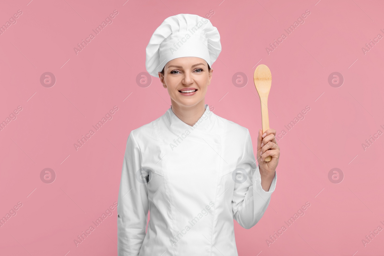 Photo of Happy chef in uniform holding wooden spoon on pink background