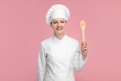 Photo of Happy chef in uniform holding wooden spoon on pink background