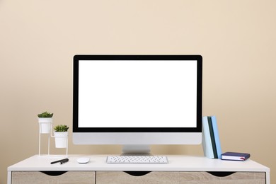 Photo of Comfortable workplace with blank computer display on desk near beige wall. Space for text
