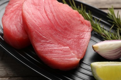 Raw tuna fillets with shallot and lime wedge on black plate, closeup