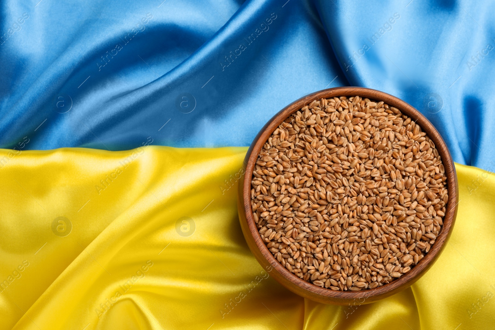 Photo of Bowl of wheat grains on Ukrainian flag, top view. Space for text