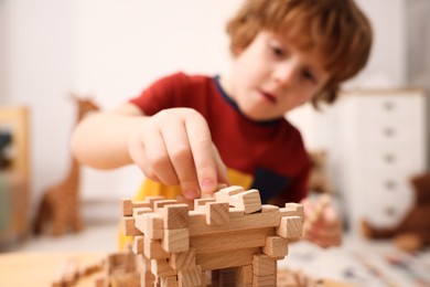 Photo of Little boy playing with wooden construction set at table in room, selective focus. Child's toy