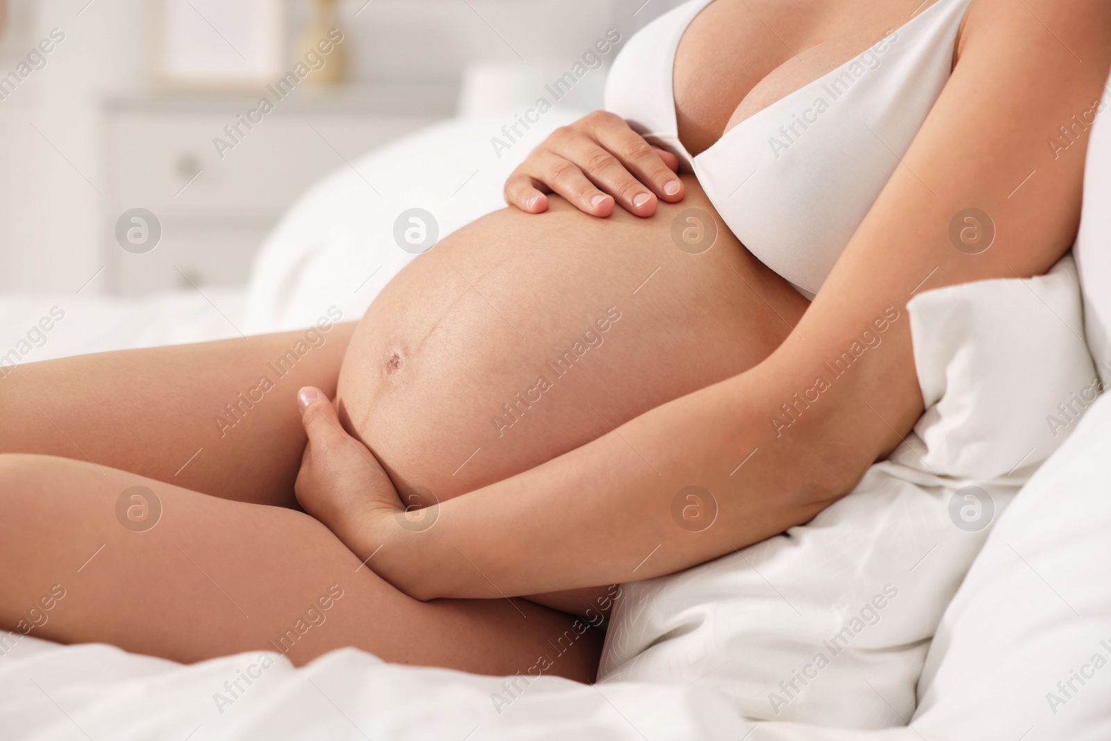 Photo of Pregnant woman in stylish comfortable underwear on bed at home, closeup