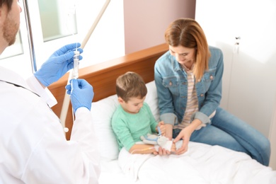 Photo of Doctor adjusting intravenous drip for little child in hospital during parent's visit
