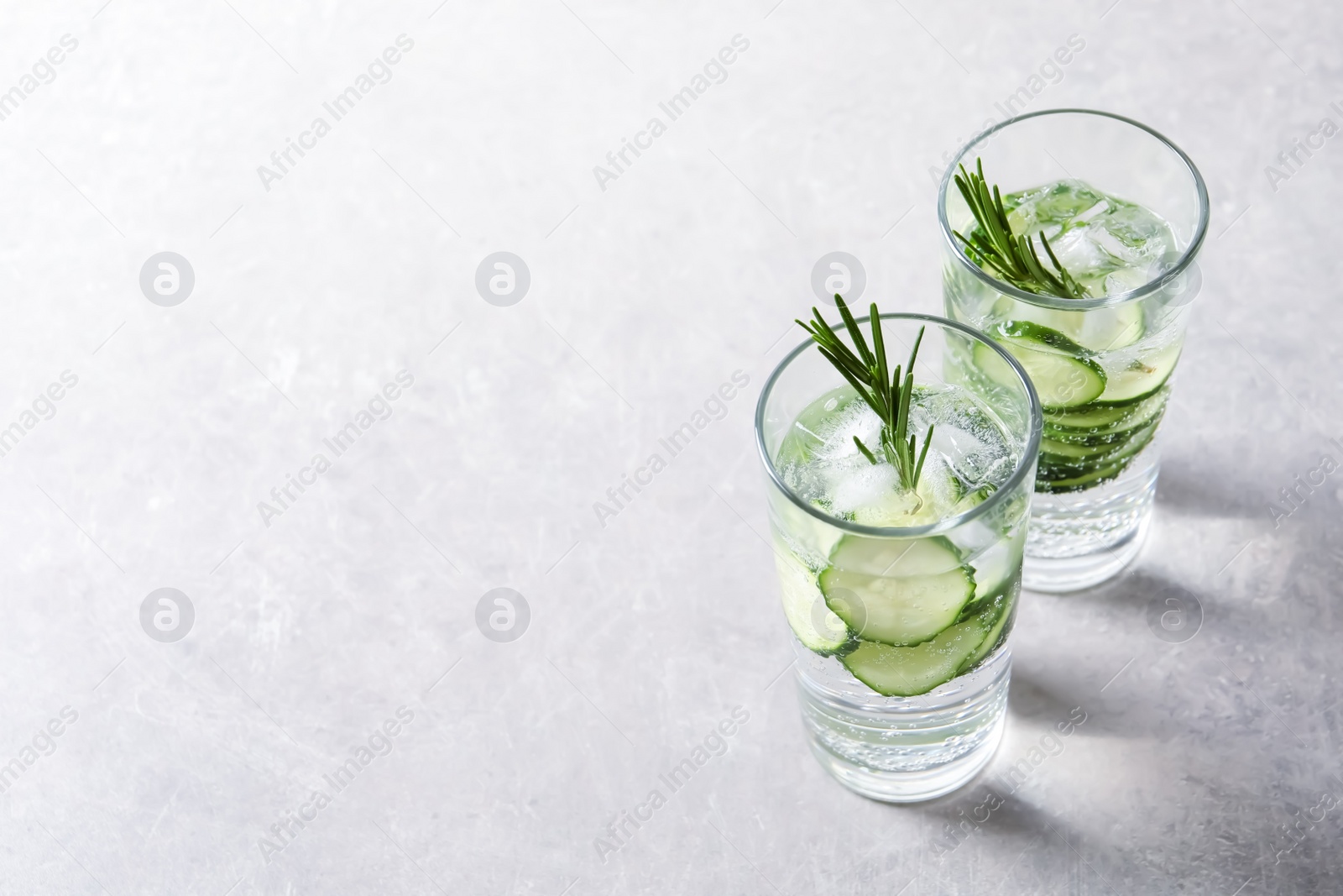 Photo of Glasses of fresh cucumber water on grey background. Space for text